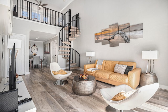 living room with hardwood / wood-style flooring, ceiling fan, crown molding, and a high ceiling