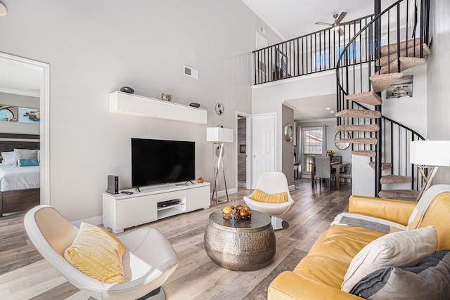 living room with ceiling fan, wood-type flooring, a high ceiling, and ornamental molding