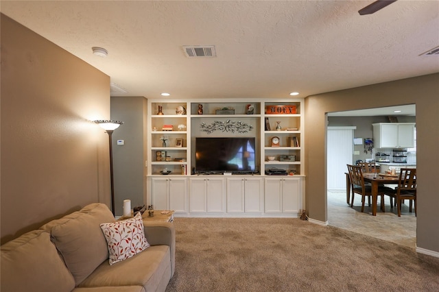 living room featuring a textured ceiling, built in shelves, ceiling fan, and light carpet