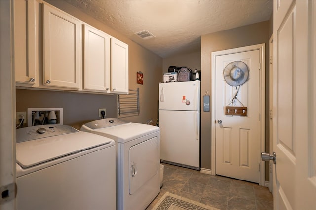 clothes washing area with cabinets, a textured ceiling, and washing machine and clothes dryer