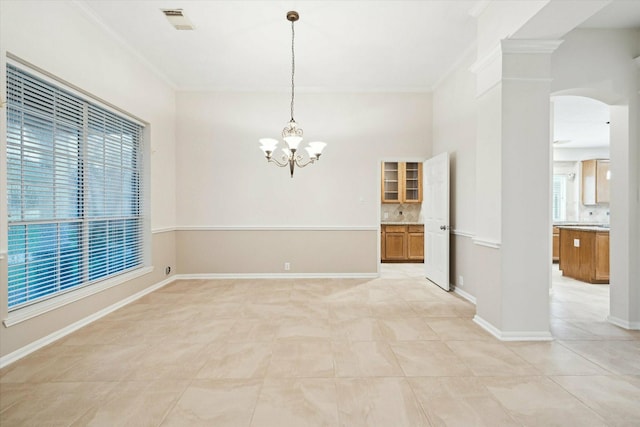 tiled spare room with a chandelier, ornate columns, and ornamental molding