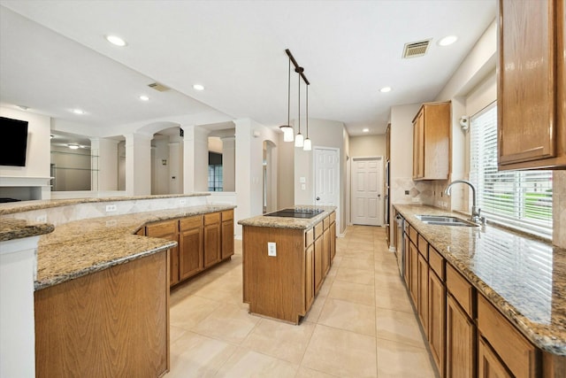 kitchen with sink, light stone countertops, black electric cooktop, decorative light fixtures, and a kitchen island