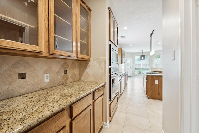 kitchen with light stone countertops, hanging light fixtures, backsplash, light tile patterned flooring, and appliances with stainless steel finishes