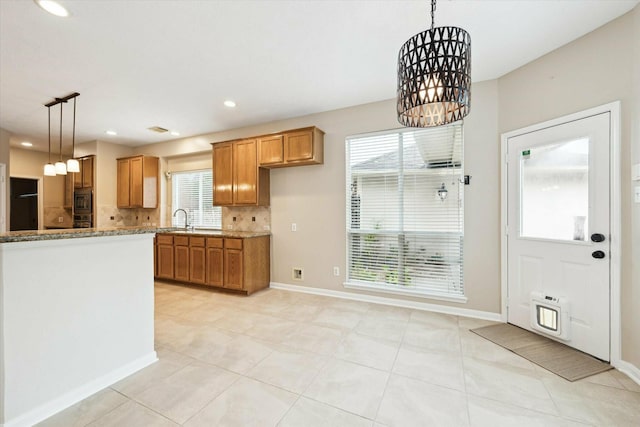 kitchen with tasteful backsplash, a healthy amount of sunlight, sink, pendant lighting, and an inviting chandelier