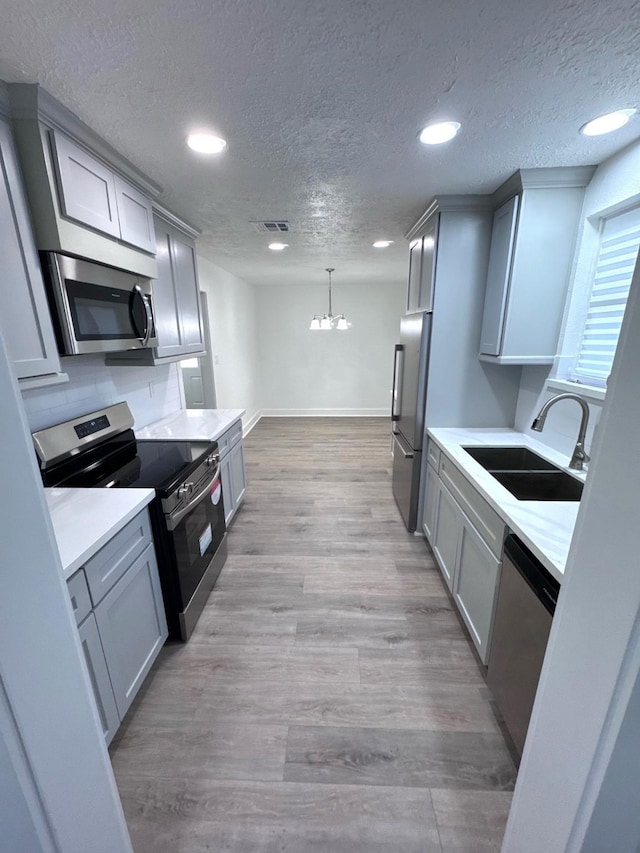 11722 Chadbrook Ln, Houston, TX 77099 - kitchen with stainless steel appliances, a sink, gray cabinets, a textured ceiling, and a chandelier