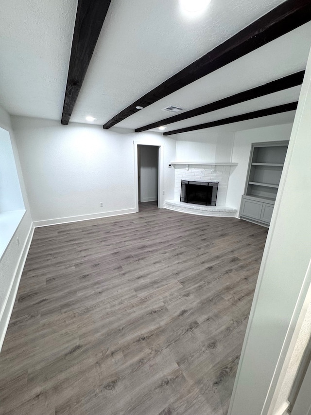 unfurnished living room with a fireplace, beamed ceiling, a textured ceiling, built in features, and hardwood / wood-style flooring