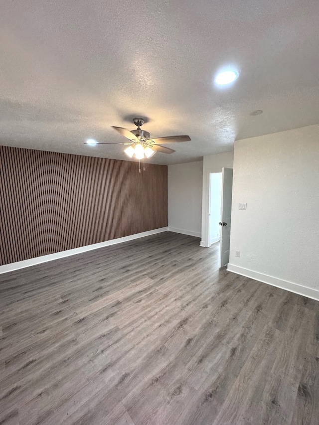 unfurnished room featuring a textured ceiling, wooden walls, dark hardwood / wood-style floors, and ceiling fan