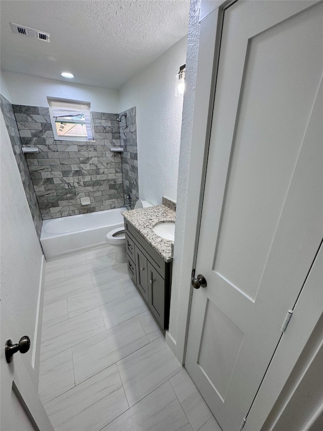 full bathroom featuring a textured ceiling, tile patterned floors, vanity, tiled shower / bath, and toilet