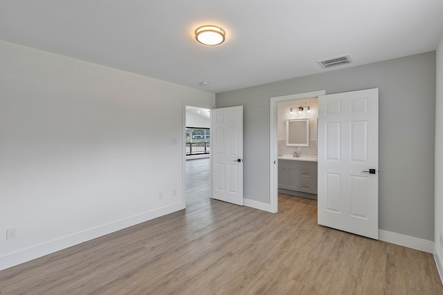 unfurnished bedroom with light wood-type flooring, sink, and ensuite bathroom