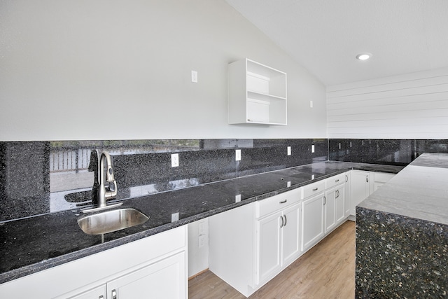 kitchen with light hardwood / wood-style floors, sink, white cabinets, lofted ceiling, and dark stone countertops