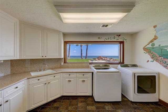 clothes washing area with a textured ceiling, washing machine and dryer, sink, and cabinets