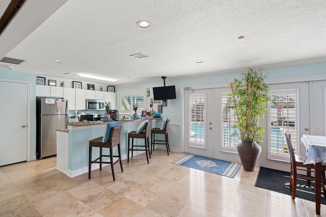 kitchen with white cabinets, kitchen peninsula, stainless steel appliances, french doors, and plenty of natural light