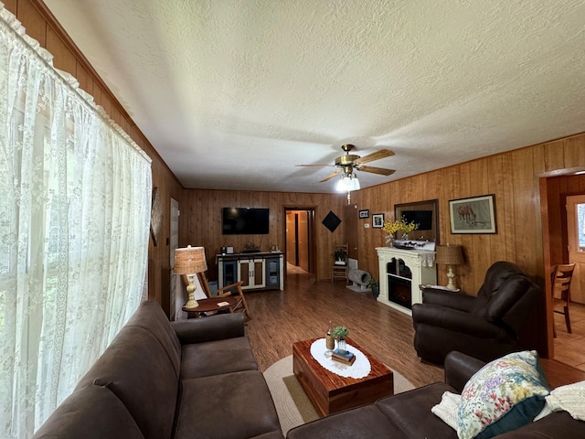 living room featuring wood walls, a ceiling fan, a fireplace, and a textured ceiling