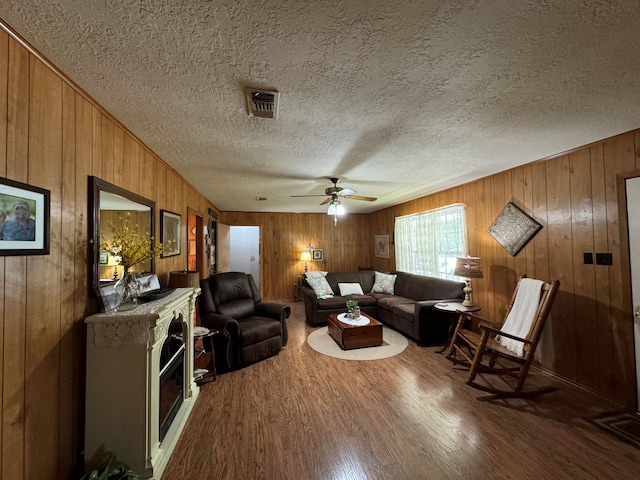 living room with a textured ceiling, wooden walls, ceiling fan, and hardwood / wood-style flooring