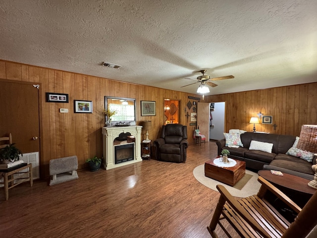 living room featuring ceiling fan, a textured ceiling, wood walls, and wood-type flooring