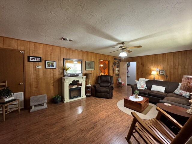 living area with a textured ceiling, a ceiling fan, visible vents, wood finished floors, and wood walls