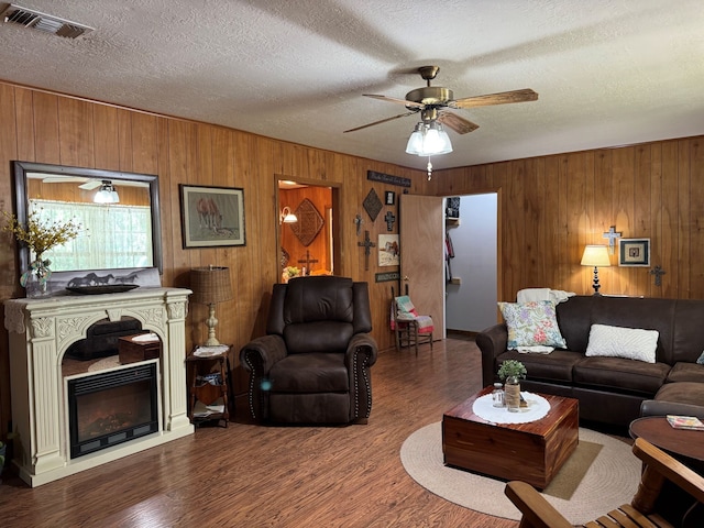 living room featuring wood walls, ceiling fan, dark wood-type flooring, and a textured ceiling