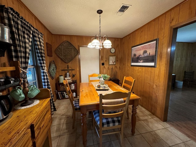 dining space featuring a chandelier, wood walls, visible vents, and light tile patterned floors