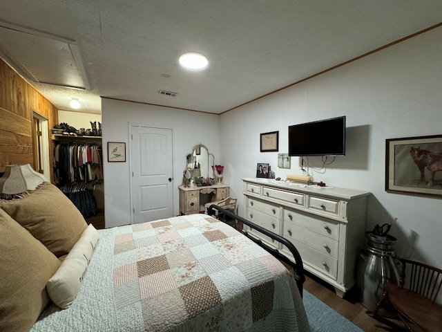 bedroom featuring a closet, a textured ceiling, dark wood-type flooring, wood walls, and a spacious closet