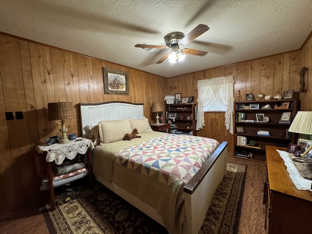 bedroom with wooden walls, ceiling fan, a textured ceiling, and dark hardwood / wood-style flooring