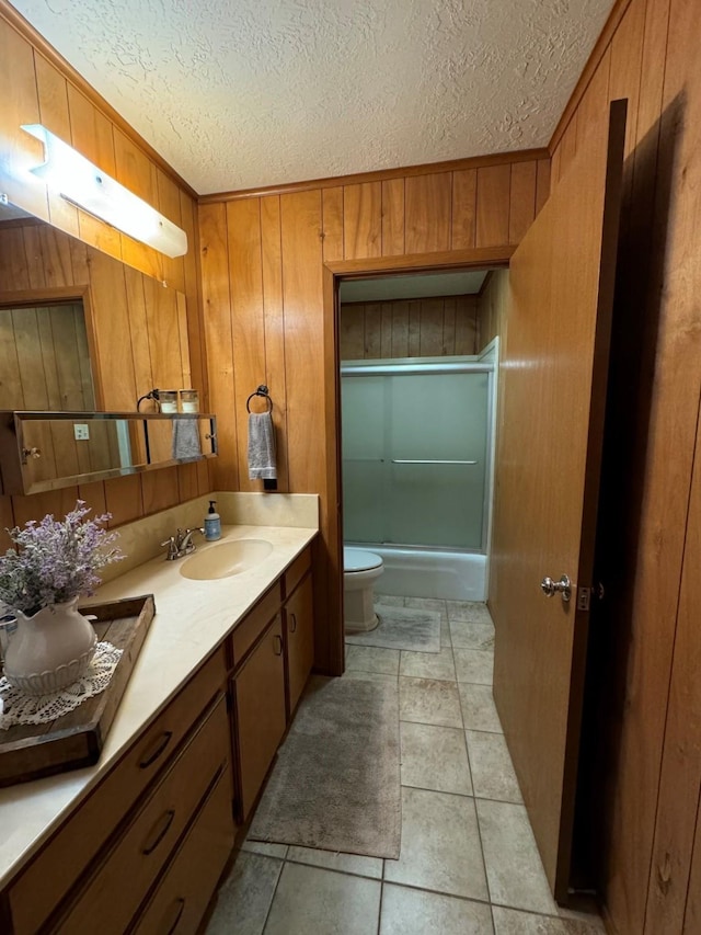 full bathroom featuring a textured ceiling, shower / bath combination with glass door, vanity, toilet, and wooden walls