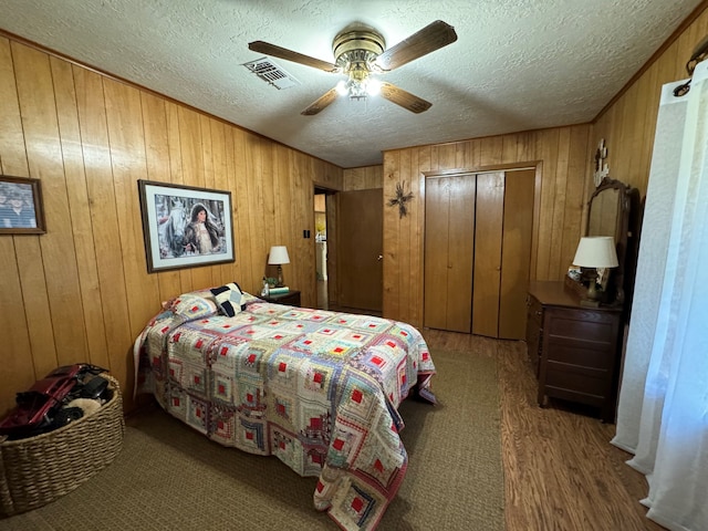 bedroom with ceiling fan, wood walls, a textured ceiling, a closet, and hardwood / wood-style floors