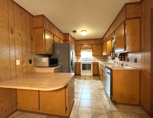 kitchen with light countertops, a textured ceiling, wood walls, stainless steel appliances, and a sink