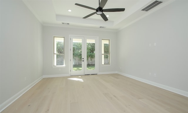 empty room with light hardwood / wood-style floors, a raised ceiling, ceiling fan, french doors, and ornamental molding