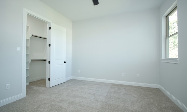 unfurnished bedroom featuring light carpet, a closet, ceiling fan, and a walk in closet