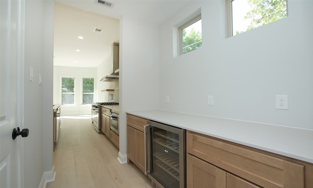 bar with beverage cooler, appliances with stainless steel finishes, plenty of natural light, and light hardwood / wood-style floors