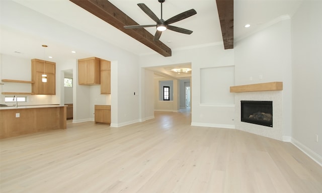 unfurnished living room featuring ceiling fan, beamed ceiling, light hardwood / wood-style floors, and a healthy amount of sunlight