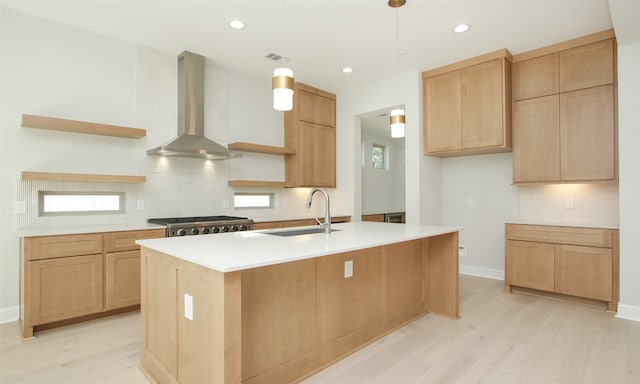 kitchen with pendant lighting, light hardwood / wood-style floors, sink, an island with sink, and wall chimney range hood