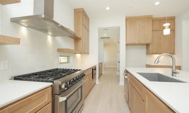 kitchen featuring sink, decorative light fixtures, wall chimney exhaust hood, appliances with stainless steel finishes, and light brown cabinetry