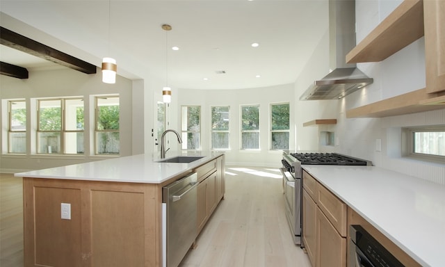 kitchen with appliances with stainless steel finishes, pendant lighting, a center island with sink, sink, and wall chimney range hood