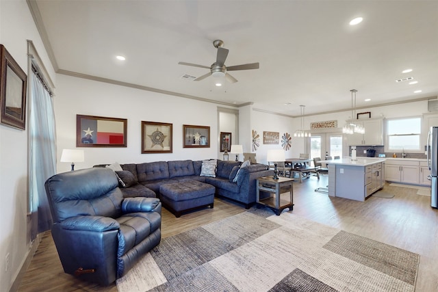 living room featuring ceiling fan with notable chandelier, light hardwood / wood-style floors, ornamental molding, and sink