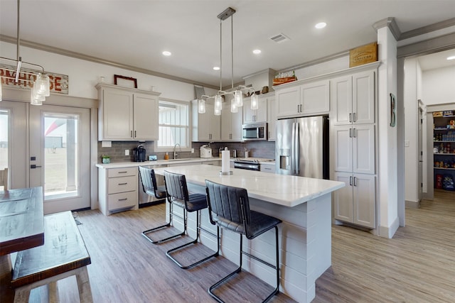 kitchen with appliances with stainless steel finishes, a kitchen island, pendant lighting, and white cabinets