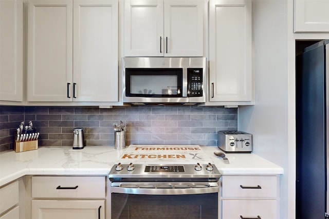 kitchen with light stone counters, white cabinets, stainless steel appliances, and decorative backsplash