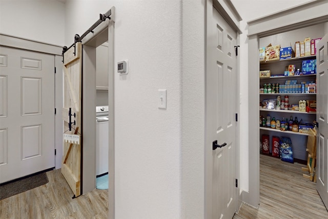 hallway with a barn door, light hardwood / wood-style floors, and washer / dryer