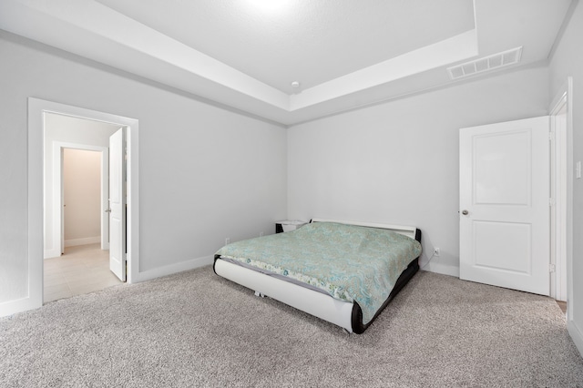 carpeted bedroom featuring ensuite bath and a raised ceiling