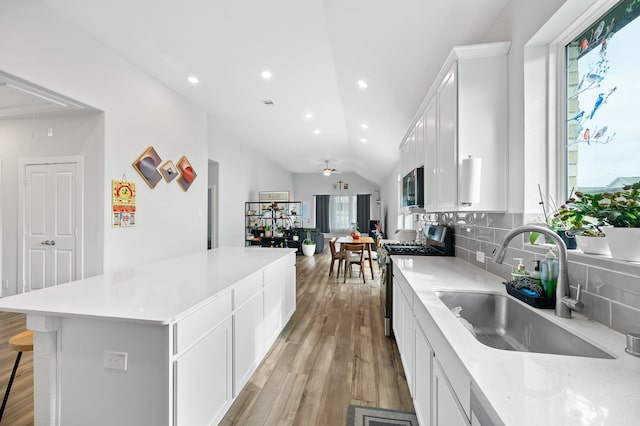 kitchen with vaulted ceiling, white cabinetry, stainless steel appliances, ceiling fan, and sink