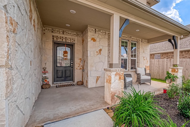 view of exterior entry with stone siding, a porch, and fence