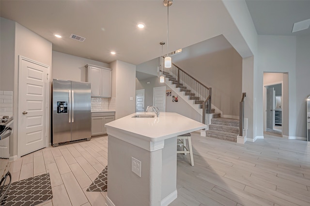 kitchen featuring stainless steel fridge, an island with sink, a breakfast bar, backsplash, and light hardwood / wood-style flooring