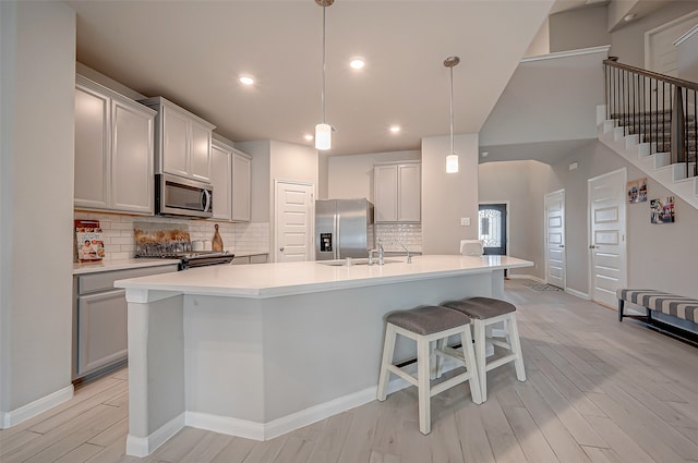 kitchen featuring an island with sink, stainless steel appliances, hanging light fixtures, and light hardwood / wood-style flooring