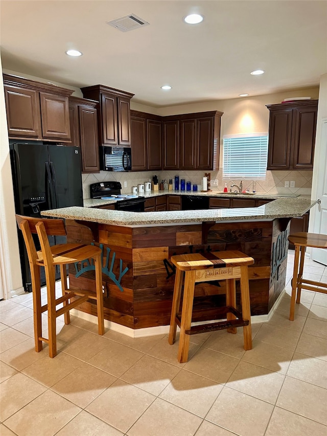 kitchen with decorative backsplash, a breakfast bar area, light tile patterned floors, black appliances, and dark brown cabinetry