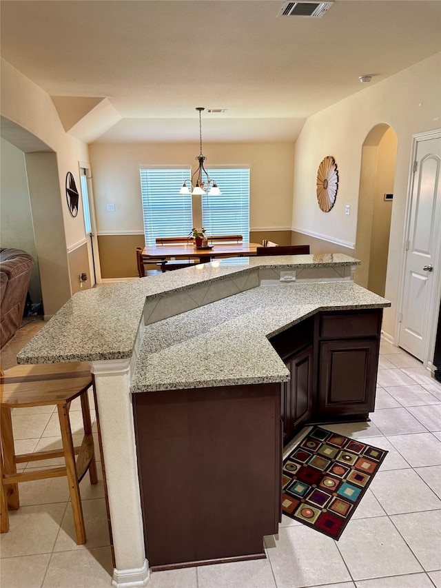 kitchen featuring light stone counters, pendant lighting, a kitchen bar, an inviting chandelier, and dark brown cabinetry