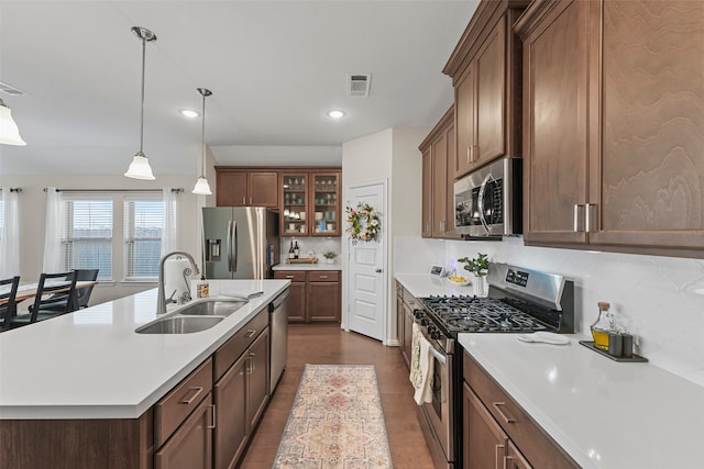 kitchen featuring tasteful backsplash, sink, stainless steel appliances, a center island with sink, and decorative light fixtures