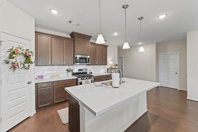 kitchen featuring appliances with stainless steel finishes, an island with sink, dark hardwood / wood-style flooring, decorative light fixtures, and sink