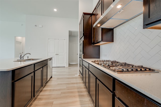 kitchen with wall chimney exhaust hood, stainless steel appliances, light hardwood / wood-style flooring, dark brown cabinetry, and sink