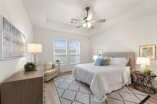 bedroom with light hardwood / wood-style floors, a raised ceiling, and ceiling fan