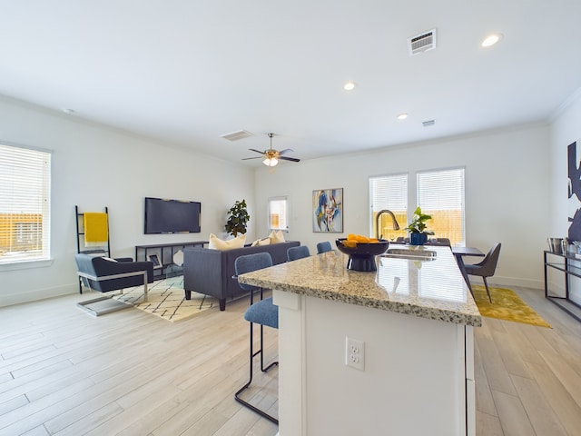 kitchen featuring light wood-type flooring, ornamental molding, ceiling fan, and an island with sink